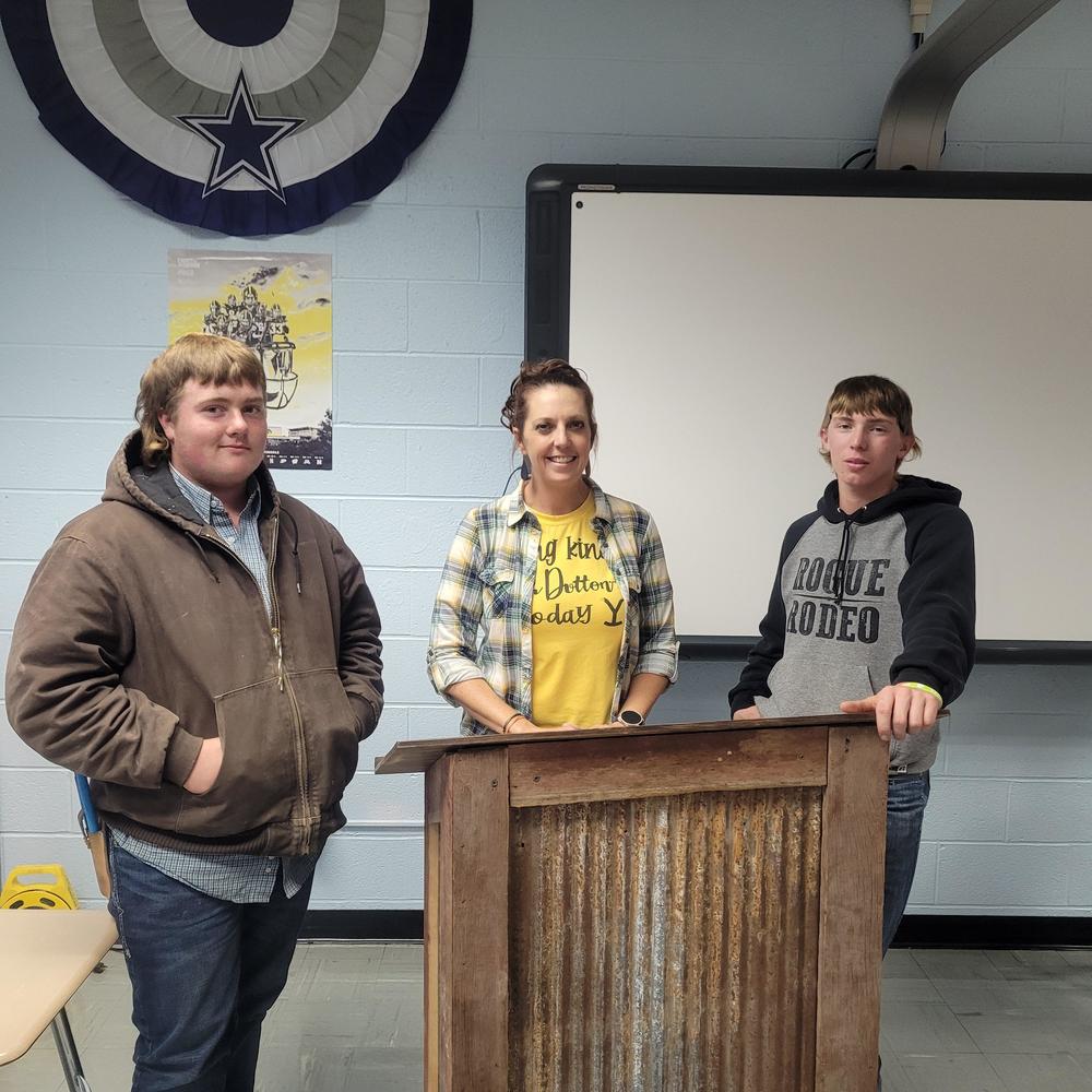 Picture of two EBF high school students with teacher, Jerri Eakes, and the podium they made for her